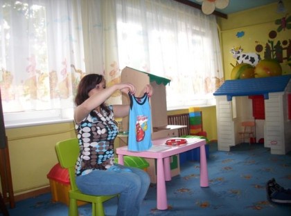 wychowawczyni w przedszkolu demonstruje jak składać koszulkę 