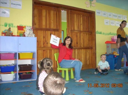 opiekunka siedząca obok dużych drewnianych drzwi i pokazująca dzieciom kartki z obrazkami