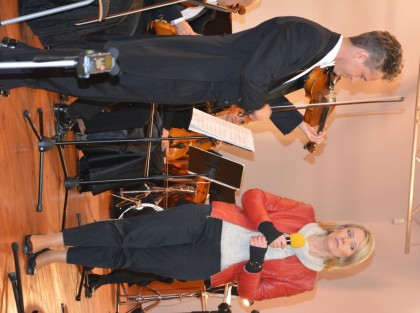 kobieta w czerwonej kurtce stoi obok muzyka grającego na skrzypcach