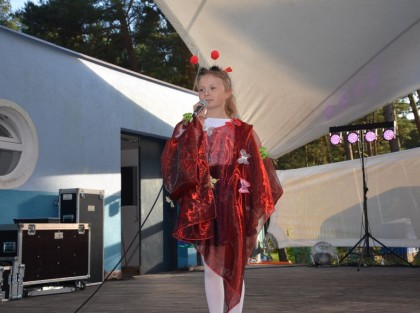 młoda dziewczynka śpiewa na scenie w czerwonej sukience