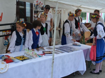 dzieci i dorośli przebrani w regionalne stroje stoją obok stołów